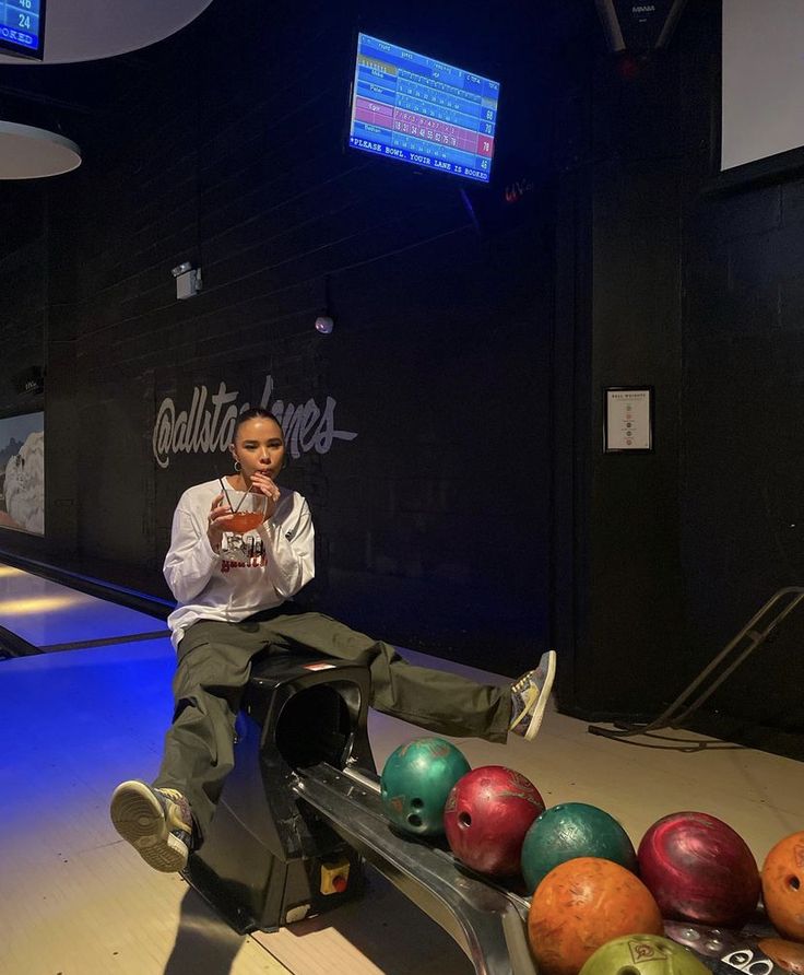 a person sitting on a bench with bowling balls in front of them and an advertisement behind them