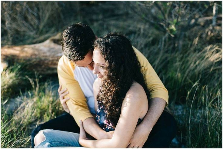 a man and woman sitting on the ground hugging each other with grass in the background