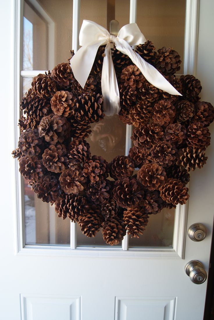 a wreath made out of pine cones is hanging on the front door with a bow