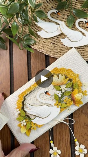 a woman is cutting paper with scissors on a table next to flowers and two swans