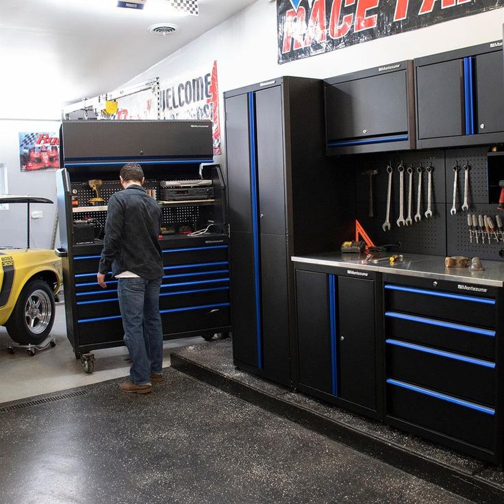 a man standing next to a yellow car in a room filled with cabinets and tools