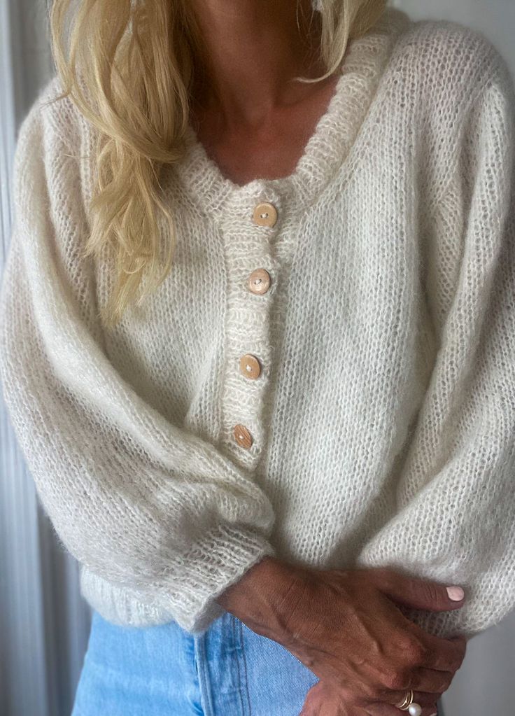 a woman wearing a white sweater and blue jeans is posing for the camera with her hands in her pockets