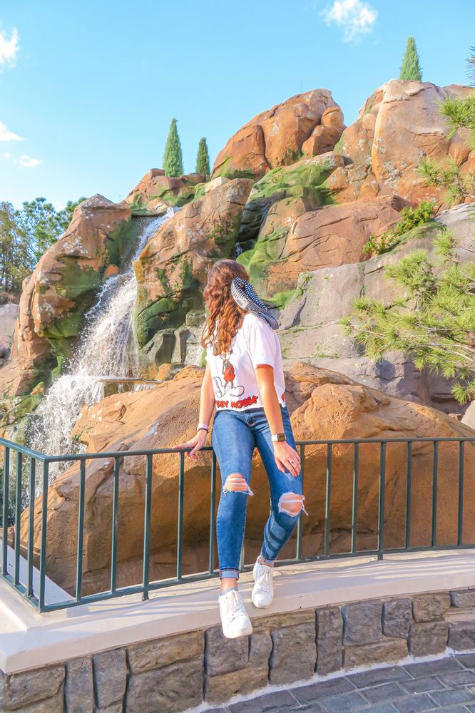 a woman standing on top of a stone wall next to a waterfall