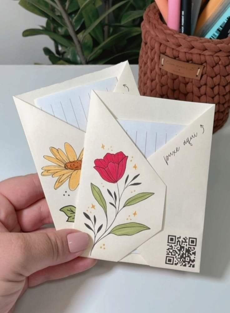 someone is holding up some envelopes that have flowers on them and are next to a potted plant