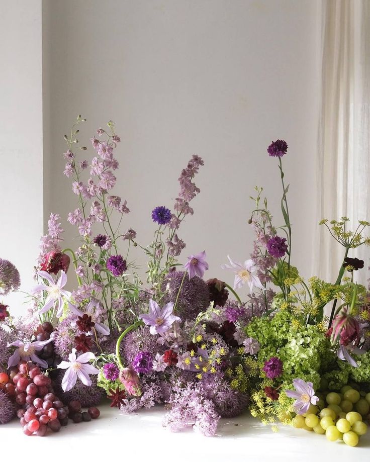 a bunch of flowers sitting on top of a table next to grapes and lemons