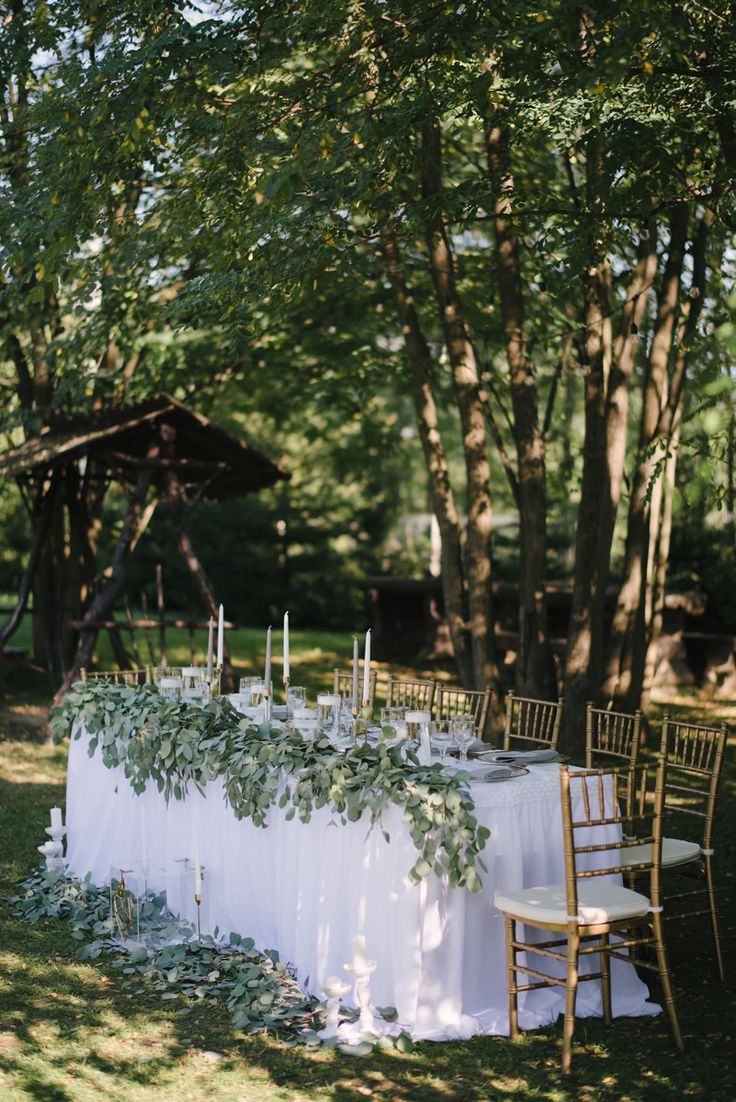 an outdoor table set up with white linens and greenery for a wedding reception