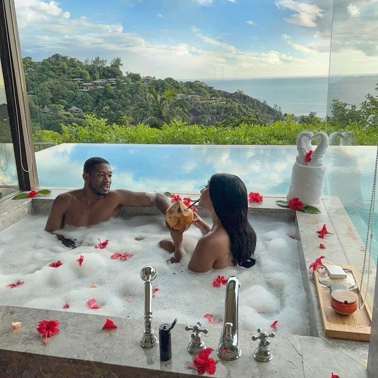 a man and woman sitting in a jacuzzi tub with flowers on the floor