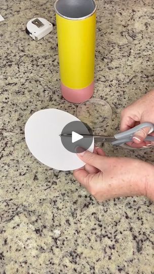 a person cutting up paper with scissors on top of a granite countertop next to a yellow cup