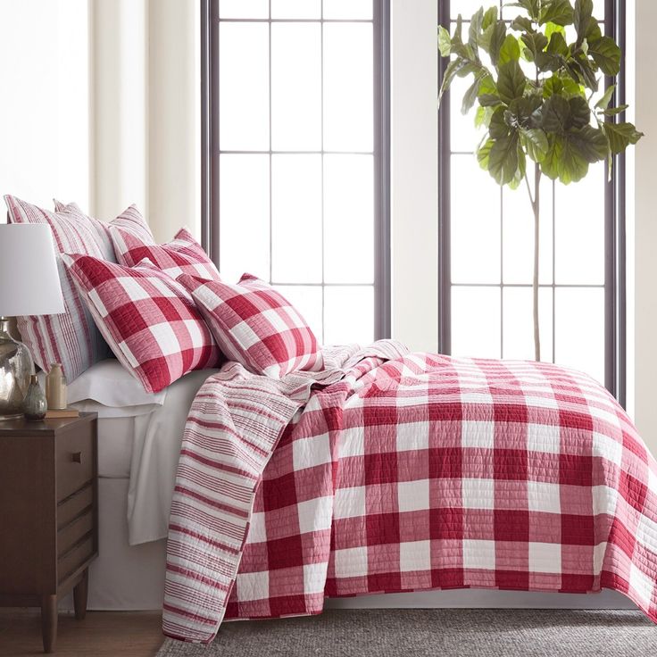 a red and white checkered bedspread on a bed in a room with large windows