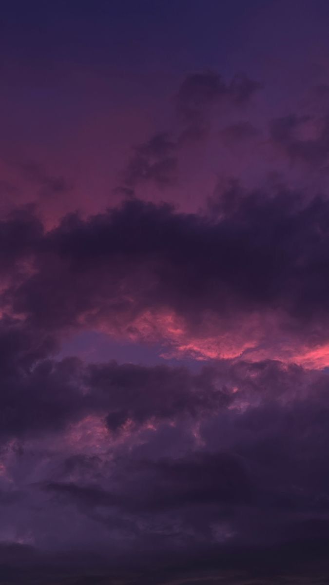 an airplane is flying in the sky at night with clouds and purple hues behind it