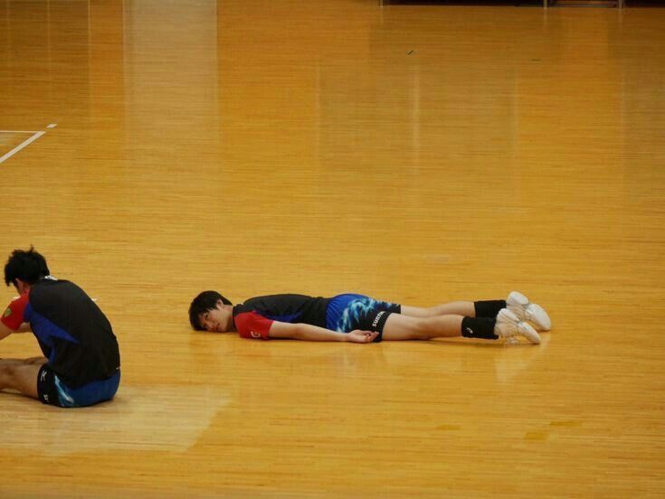 two men are laying on the floor in a gym and one is holding a ball