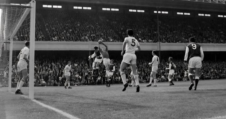 a group of men playing soccer in front of an audience at a sporting event, during the 1950's