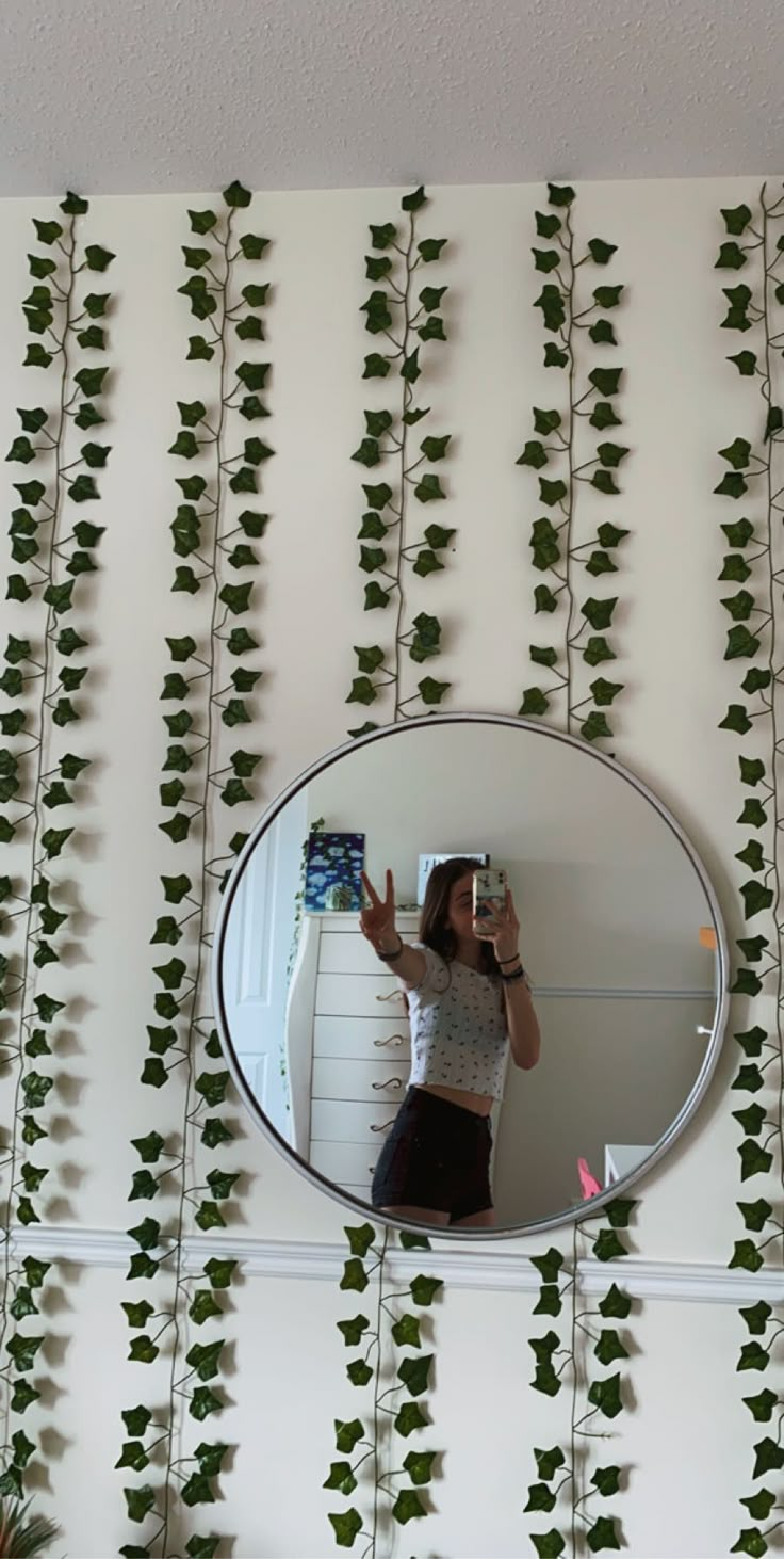 a woman taking a selfie in front of a mirror with ivy growing on it