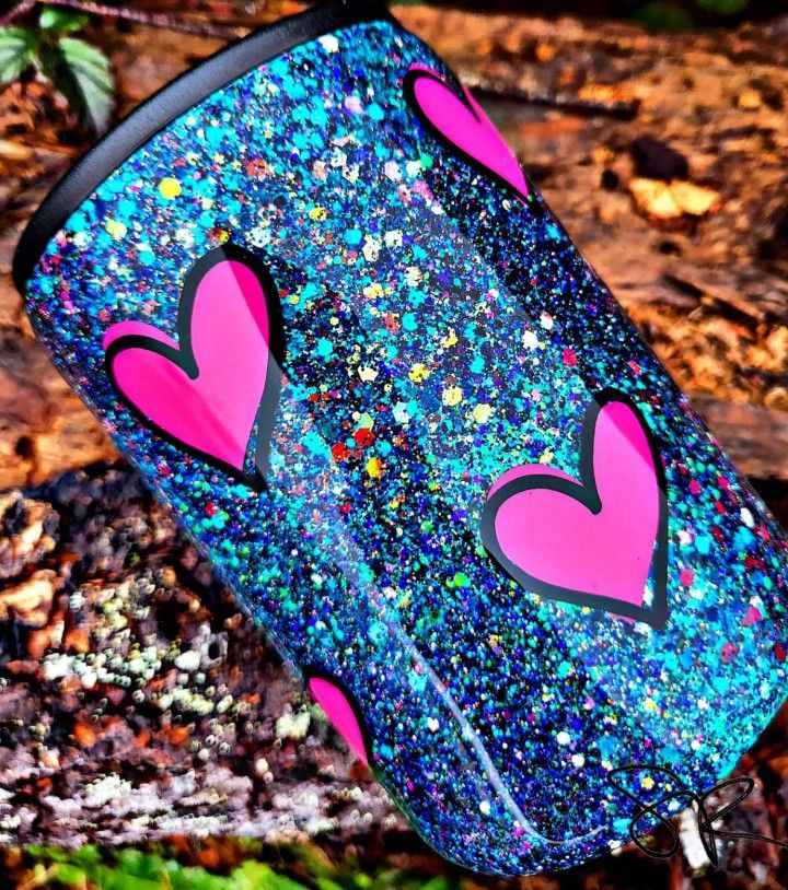 a blue and pink cup with hearts painted on it in the woods next to leaves