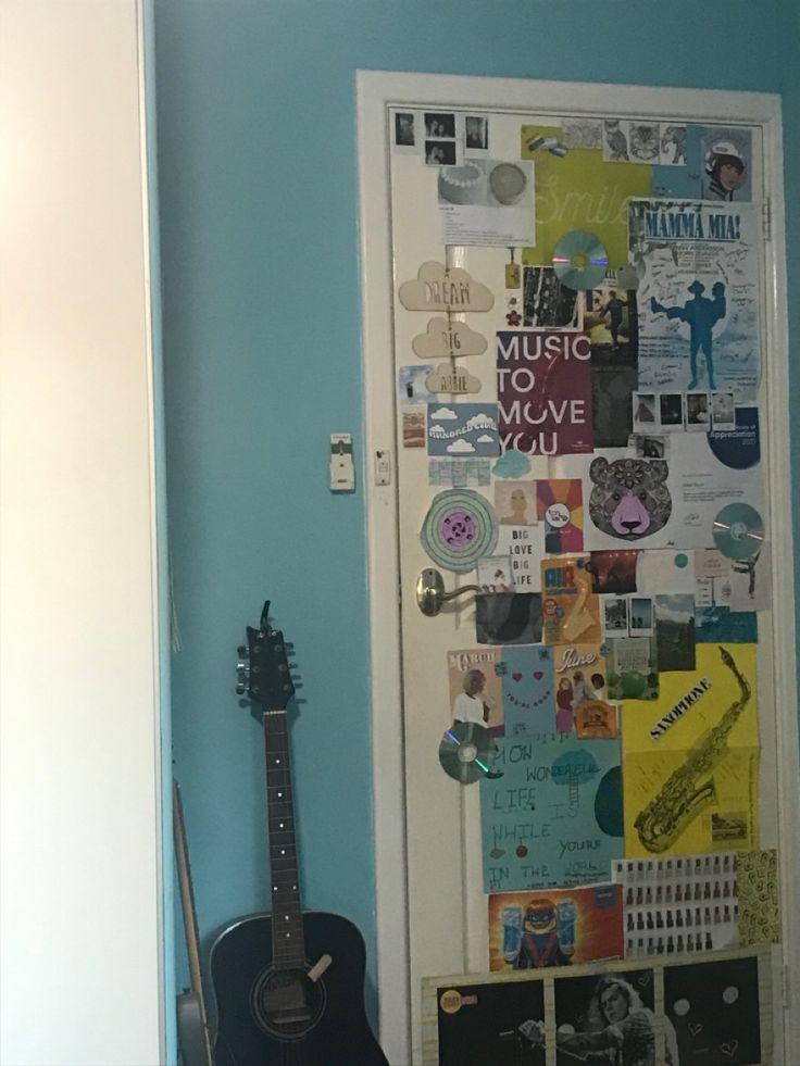 a guitar sitting in front of a door covered with pictures and magnets on it