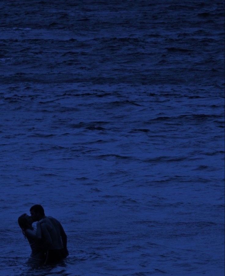 a man standing in the ocean at night with his arm around another man's head