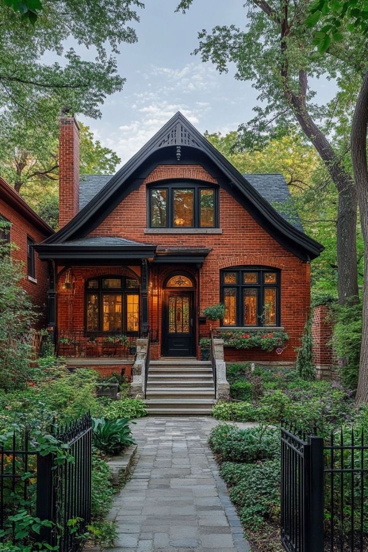 a red brick house surrounded by trees and bushes with black iron fence around the front door