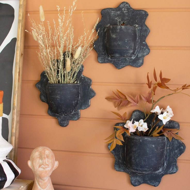 three pots with flowers are hanging on the wall next to a statue and other decorative items