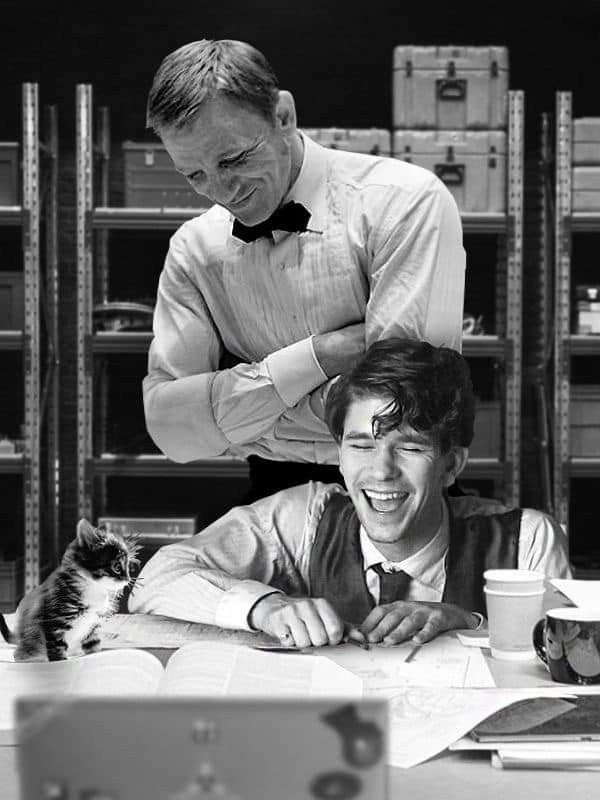 two men are working at a desk with a cat in front of them and one man is smiling