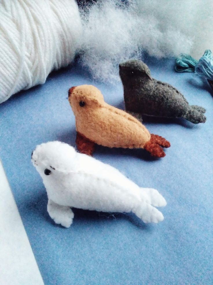 three small stuffed animals sitting on top of a blue surface next to white yarn and balls of thread