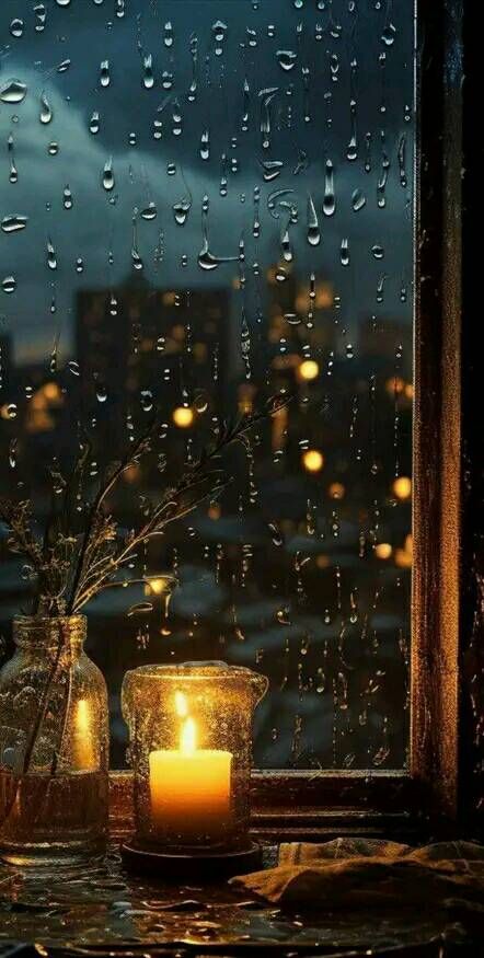 two candles are sitting on a table in front of a window with raindrops