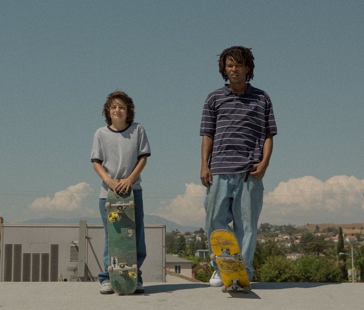 two young men standing next to each other with skateboards on their feet and one holding a skateboard