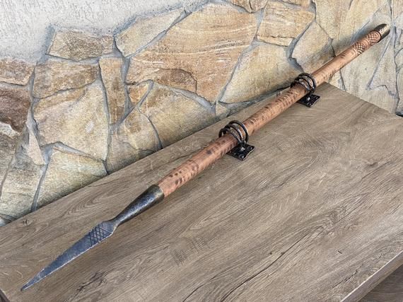 a fishing rod on top of a wooden table next to a stone wall with a knife sticking out of it