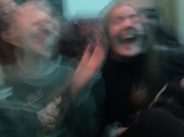 blurry photograph of two women laughing and one holding her arm up in the air