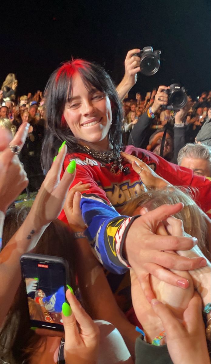 a woman is surrounded by fans and taking pictures with her cell phone at a concert