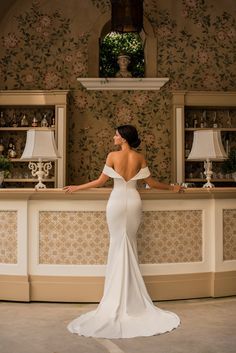 a woman standing in front of a counter wearing a white dress and looking off to the side