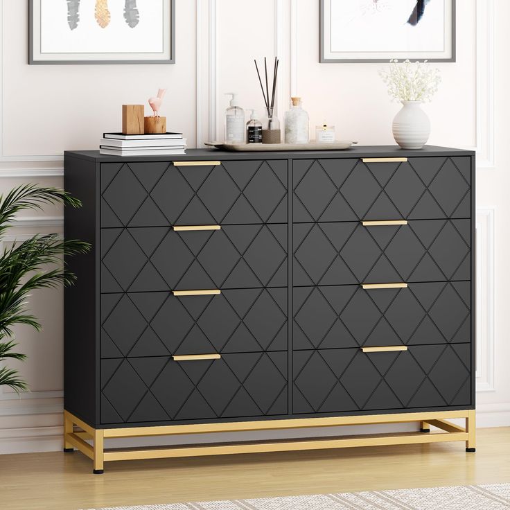 a black and gold dresser in a white room with pictures on the wall behind it