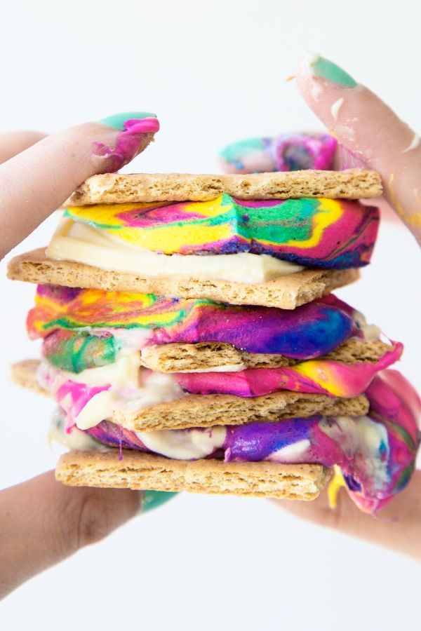 a person holding up a colorful sandwich with marshmallows and rainbow icing