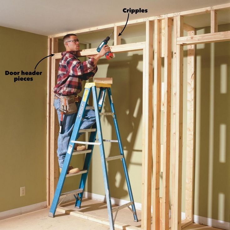 a man standing on a ladder in front of a wall that has been framed with wood