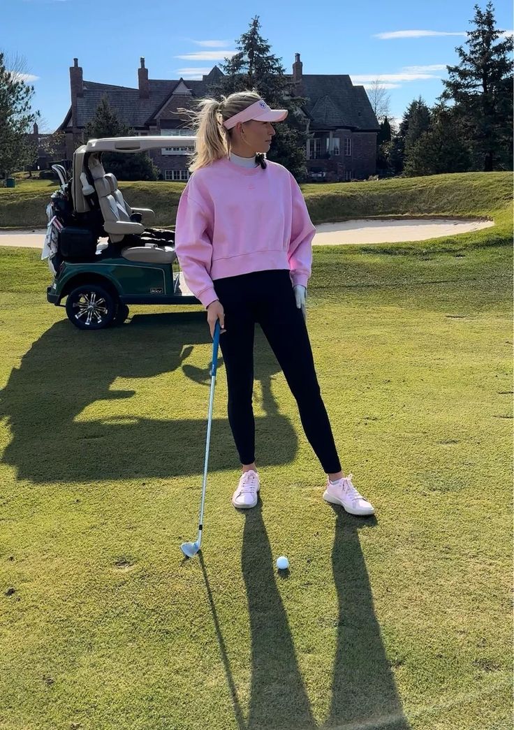 a woman in pink sweater and black pants playing golf