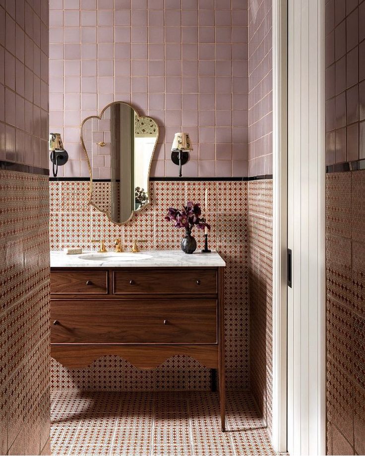 a bathroom with pink tiles on the walls and a wooden vanity topped with a mirror