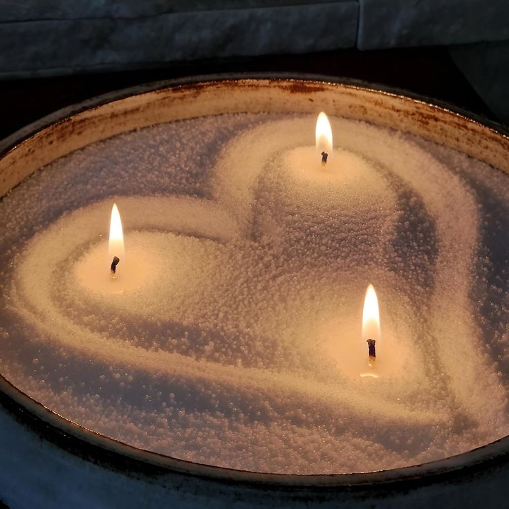 three candles are lit in the shape of a heart on a pan covered with snow