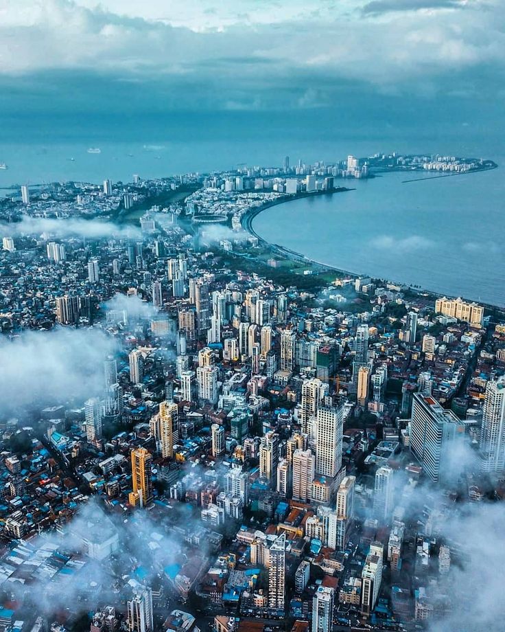 an aerial view of a city with clouds in the foreground and a body of water below