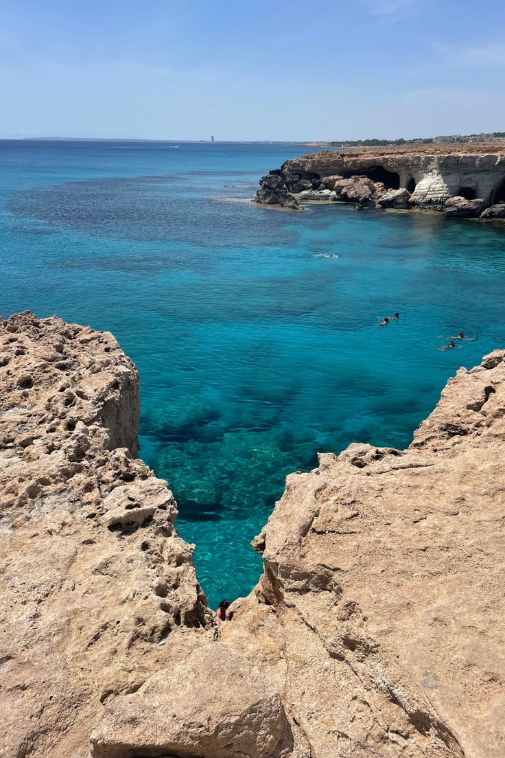 people swimming in the clear blue water near rocks