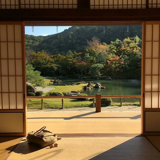 an open door leading to a small pond in a japanese garden with mountains and trees behind it