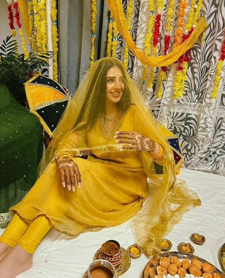 a woman dressed in yellow sitting on a bed with food and decorations around her feet