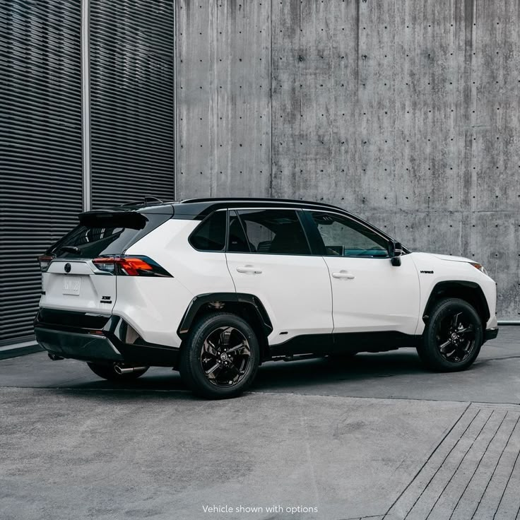 a white toyota rav parked in front of a concrete wall with black rims