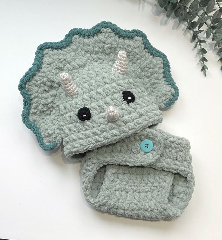 an elephant crocheted hat and booties are sitting next to a green plant