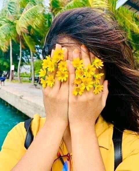 a woman covering her eyes with yellow flowers in front of her face and palm trees behind her