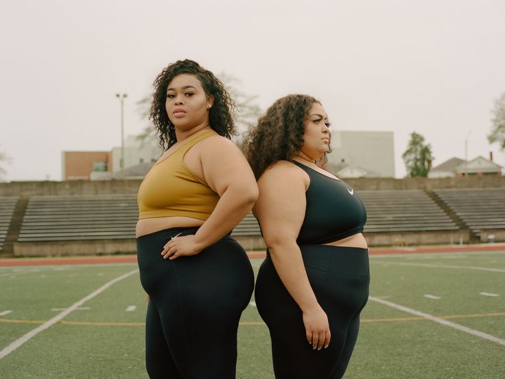 two women standing in front of a football field with their hands on their hipss