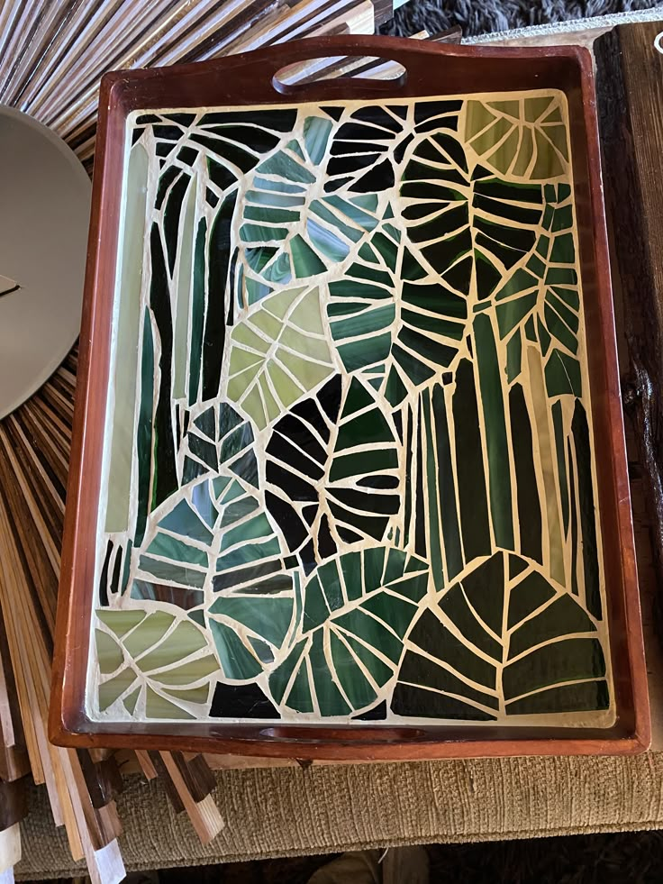 a wooden tray with stained glass designs on the bottom and sides, sitting on a table next to bamboo sticks