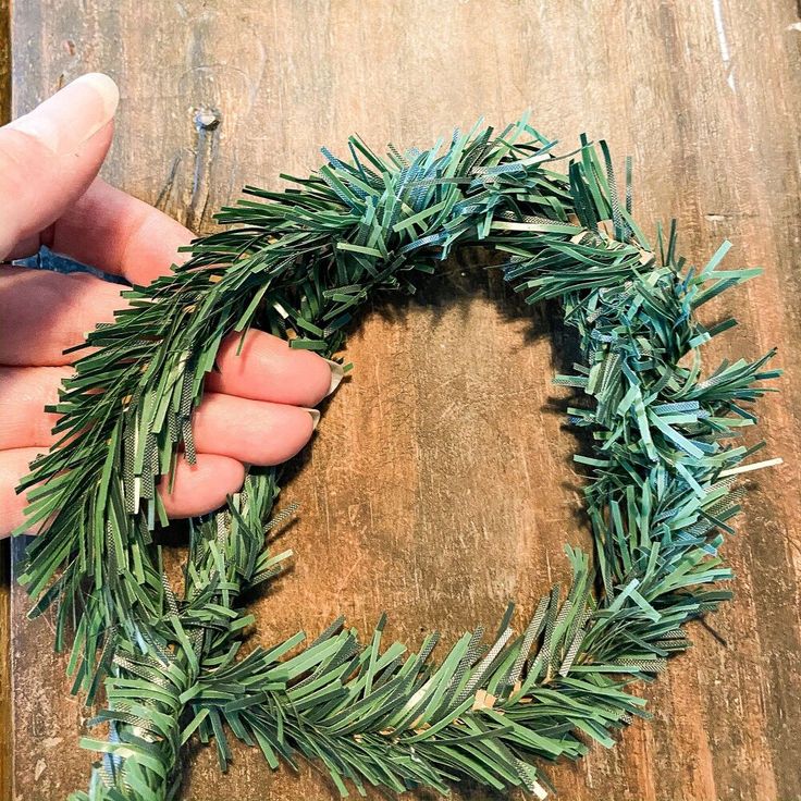 someone is making a christmas wreath out of fake greenery on a wooden table top