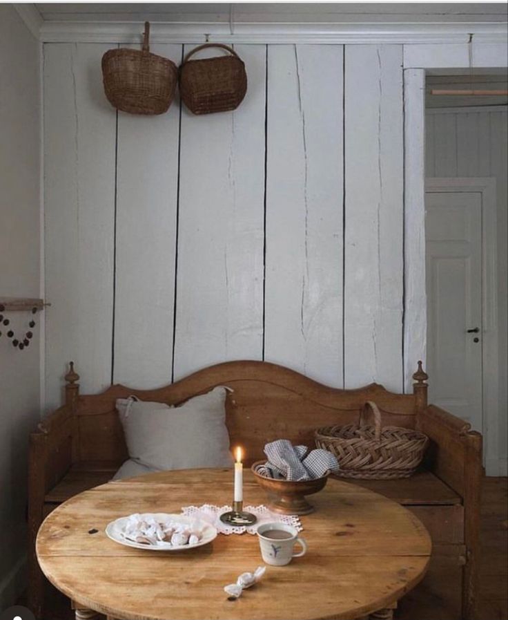 a wooden table with a candle on it in front of a white wall and basket hanging from the ceiling