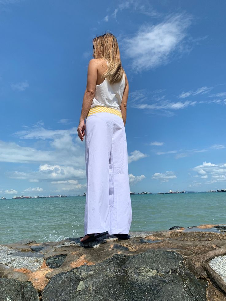 a woman standing on top of a rock next to the ocean with her hands in her pockets