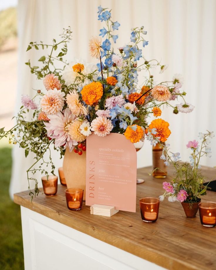 an arrangement of flowers in vases on a wooden table with candles and menu card