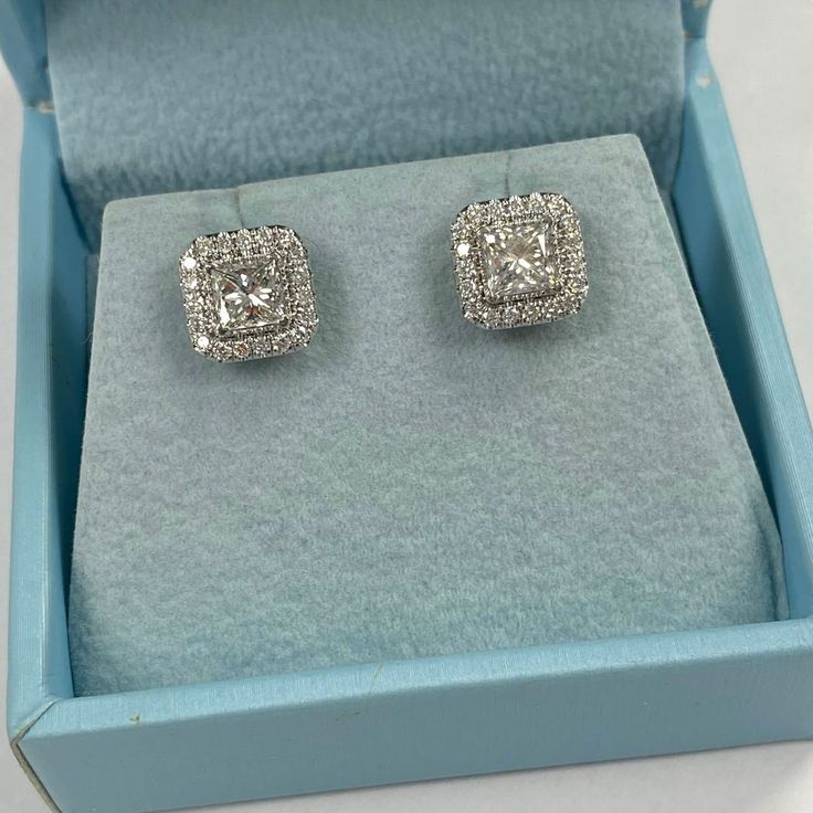 These exquisite stud earrings showcase 1.36 carats princess-cut diamonds, embraced by a halo of 0.43 carat round-cut diamonds. Designed with your comfort in mind, these stud earrings feature a screw back closure, ensuring a comfortable and worry-free wear.  Weighing 3.1 grams, these earrings are crafted from shiny 14k white gold, creating a classic and versatile setting.  With their timeless design and subtle elegance, these simple diamond stud earrings are the perfect accessory for any occasion, effortlessly adding a touch of sophistication to your ensemble.  We guarantee that all of our diamonds are 100% conflict-free. The earrings are certified by a third party gemological laboratory. Estimated Retail Value - $5750.00 Total Carat Weight - 1.79 Center Stones - 1.36 carats Princess cut ea Princess Cut Earrings Studs, Diamond White Square Cut Diamond Earrings, Diamond White Earrings With Radiant Cut Diamond Accents, Square-cut Diamond White Earrings, Radiant Cut Diamond Earrings With Diamond Accents, Radiant Cut Diamond Earrings With Accents, Square Cut Diamond White Earrings, Fine Jewelry Princess Cut Diamond Earrings With Accents, Vvs Clarity Princess Cut Diamond Earrings For Formal Occasions